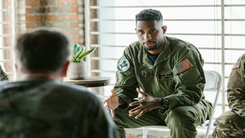 Man in slight suit speaks to group of uniformed military individuals.